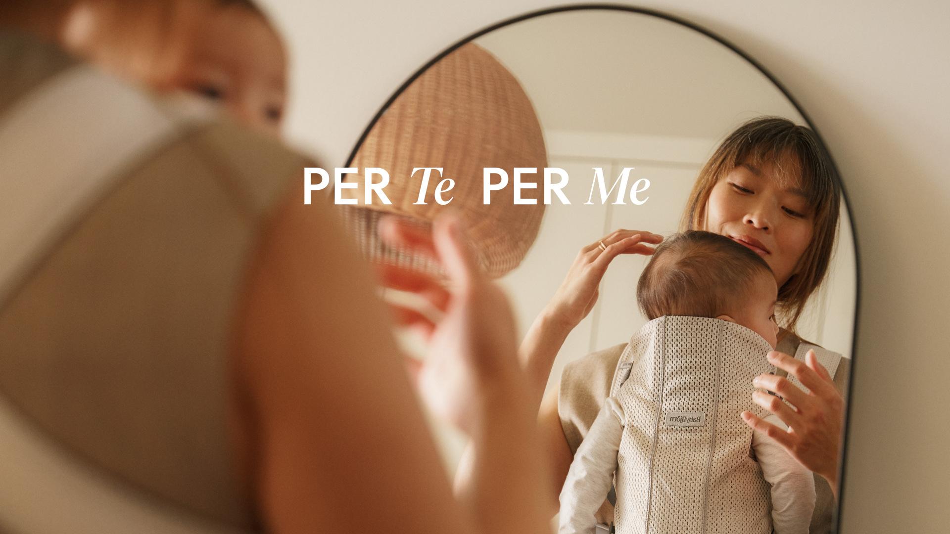 A woman holds a baby in a carrier, reflected in a mirror. Text overlay reads "PER Te PER Me." A pendant light is visible in the background.